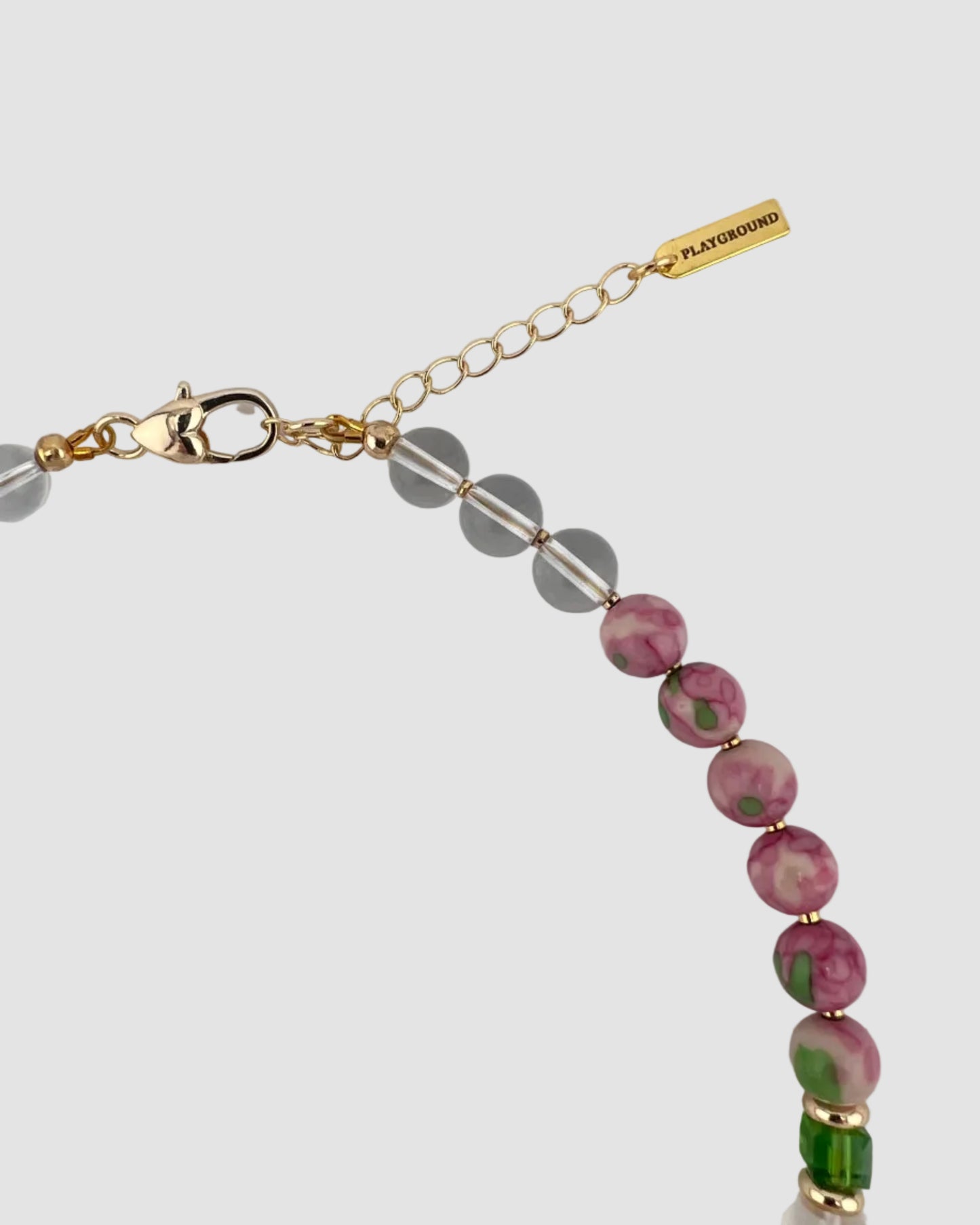 Necklace with pink and green beads and gold clasp on a light gray background