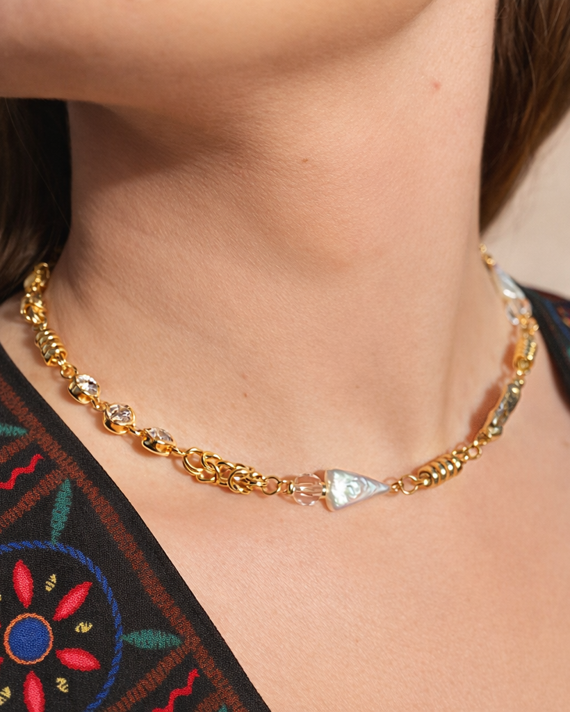 Gold necklace with a triangular pendant on a person wearing an embroidered garment.