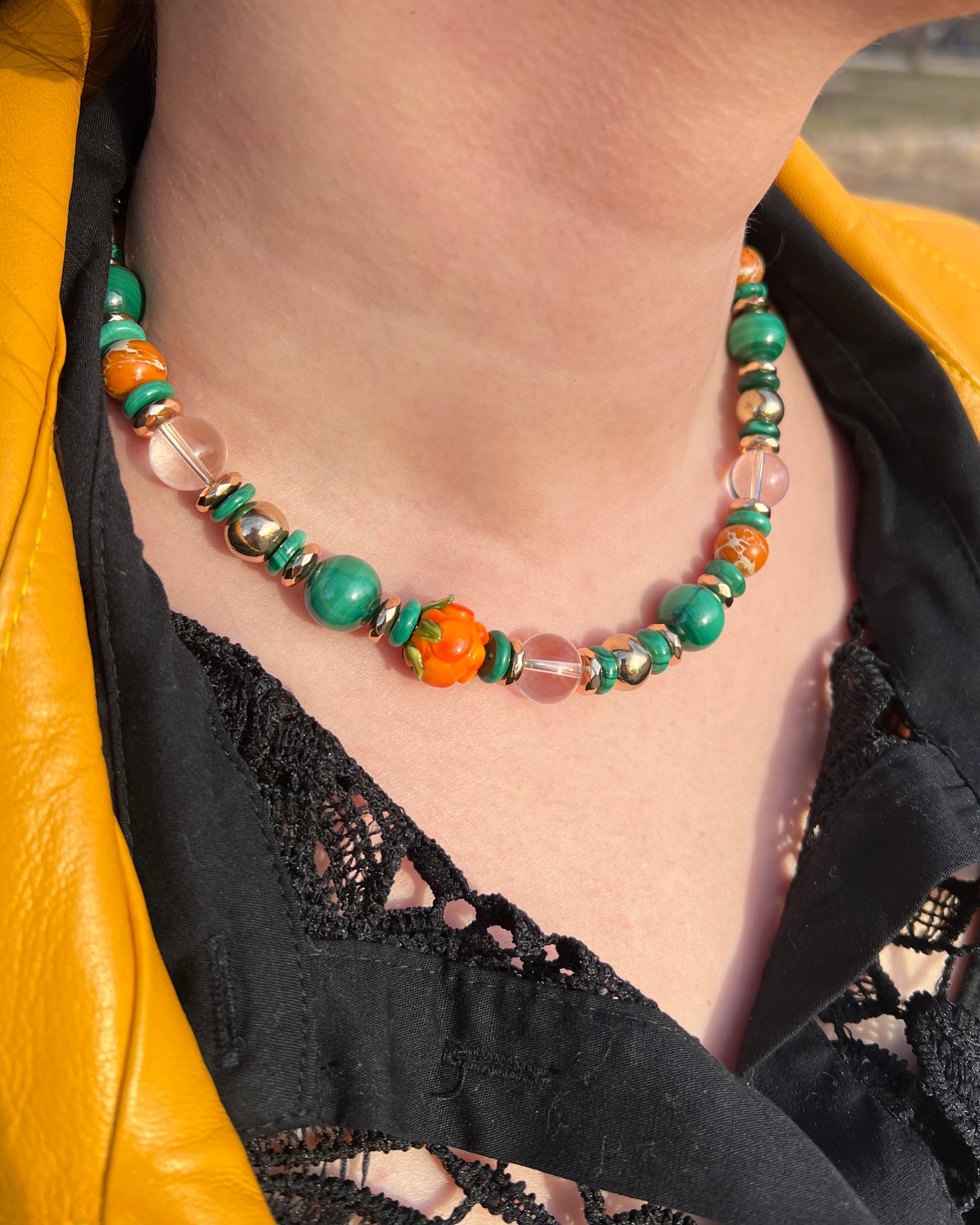Necklace with green, orange, and clear beads worn by a person in a yellow jacket.