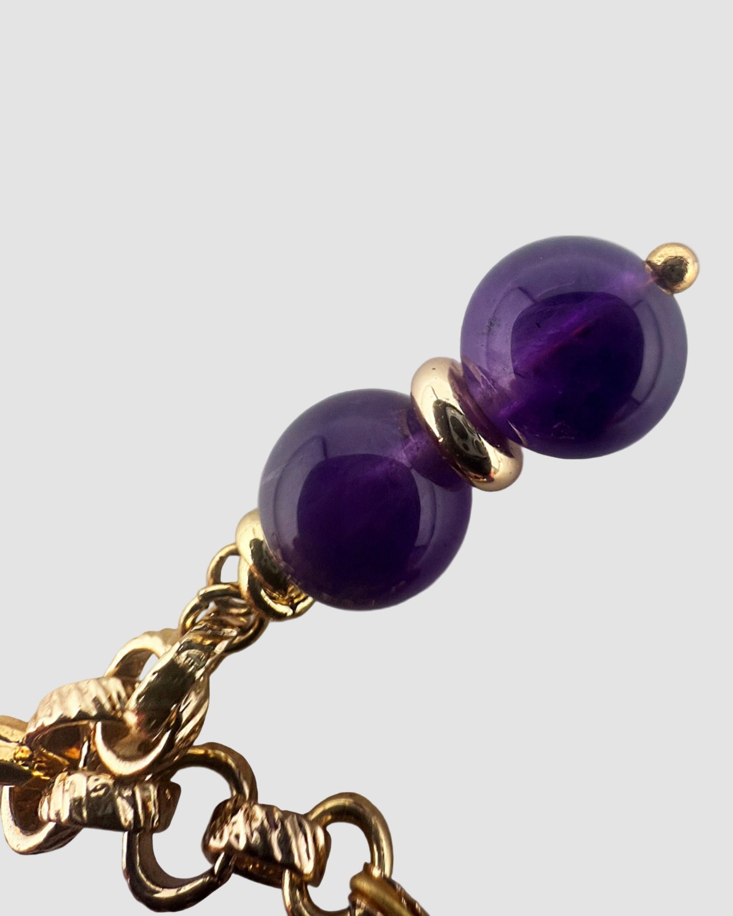 Gold chain with purple beads on a light gray background