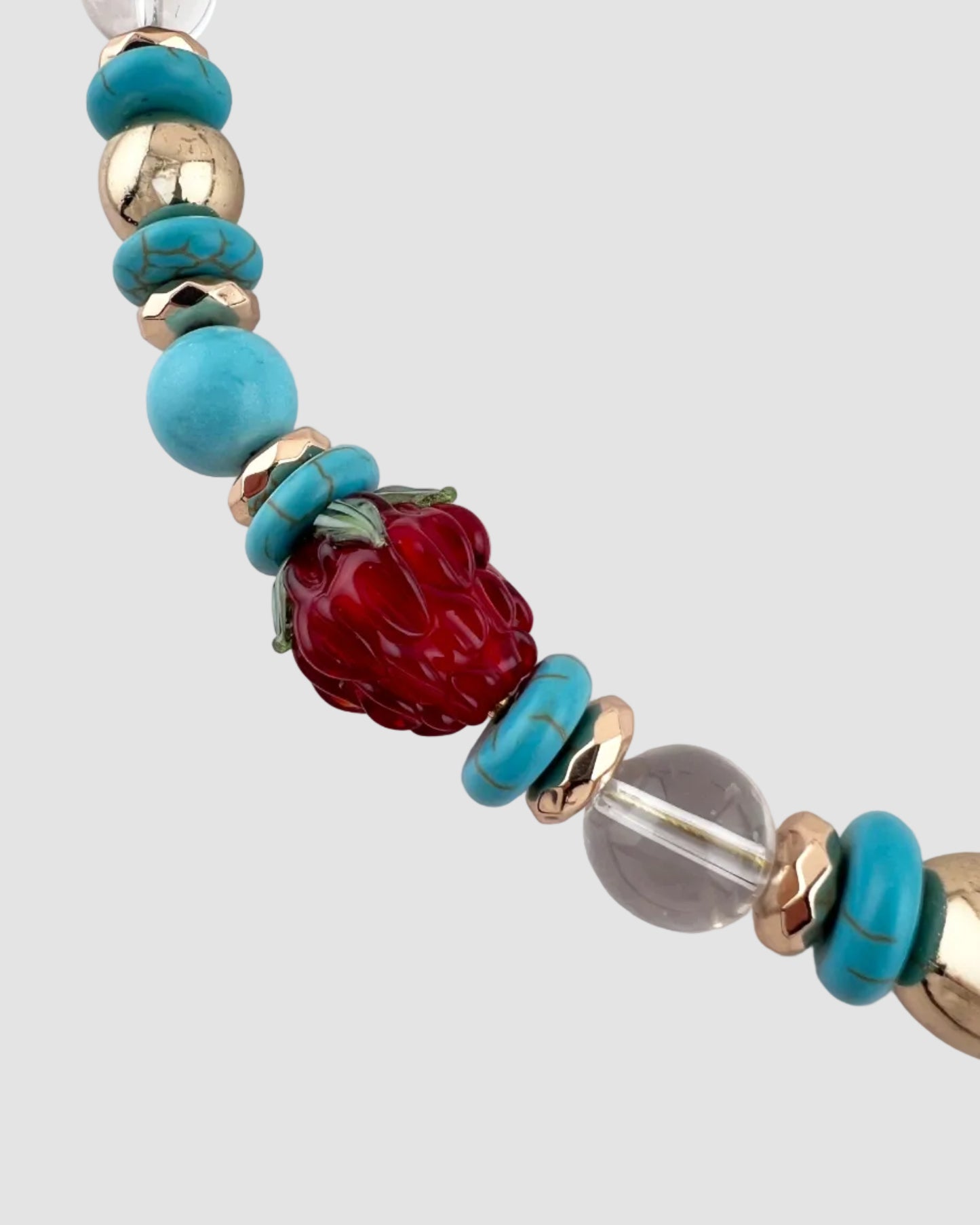 Necklace with turquoise, gold, red, and clear beads on a white background