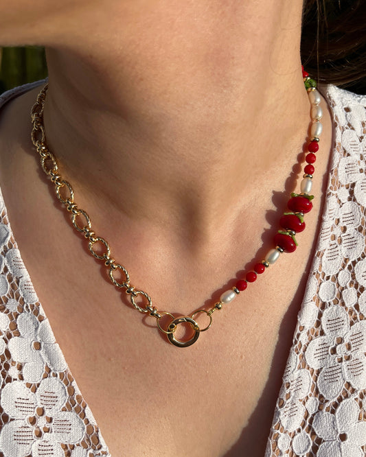 Necklace with gold chain and red tomato and pearls on a person wearing a white lace top.