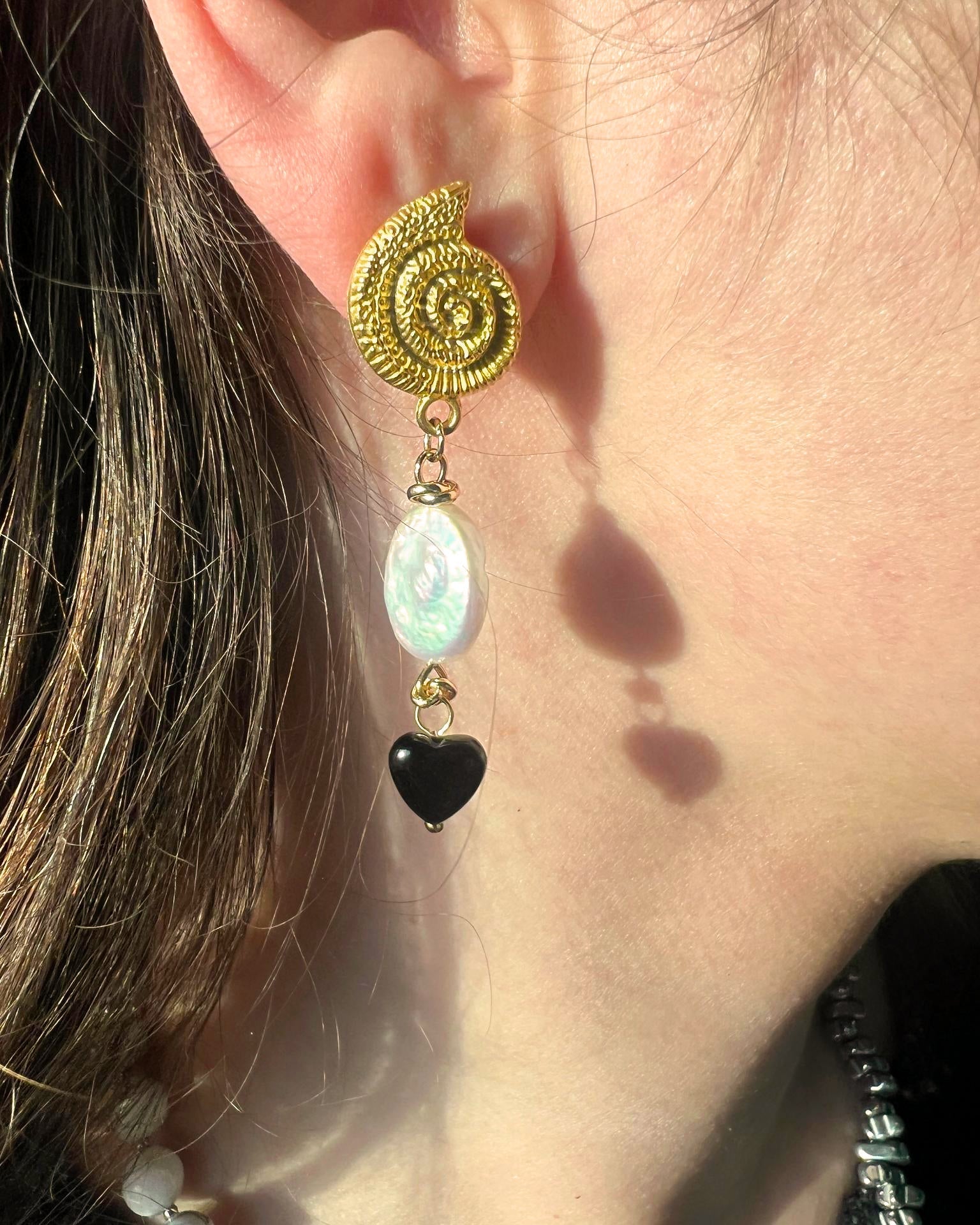 Close-up of a gold spiral earring with a black heart and white bead on an ear.