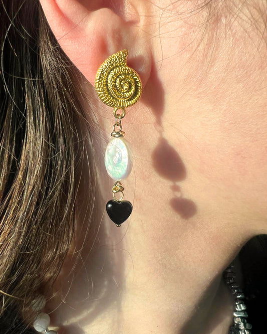 Close-up of a gold spiral earring with a black heart and white bead on an ear.