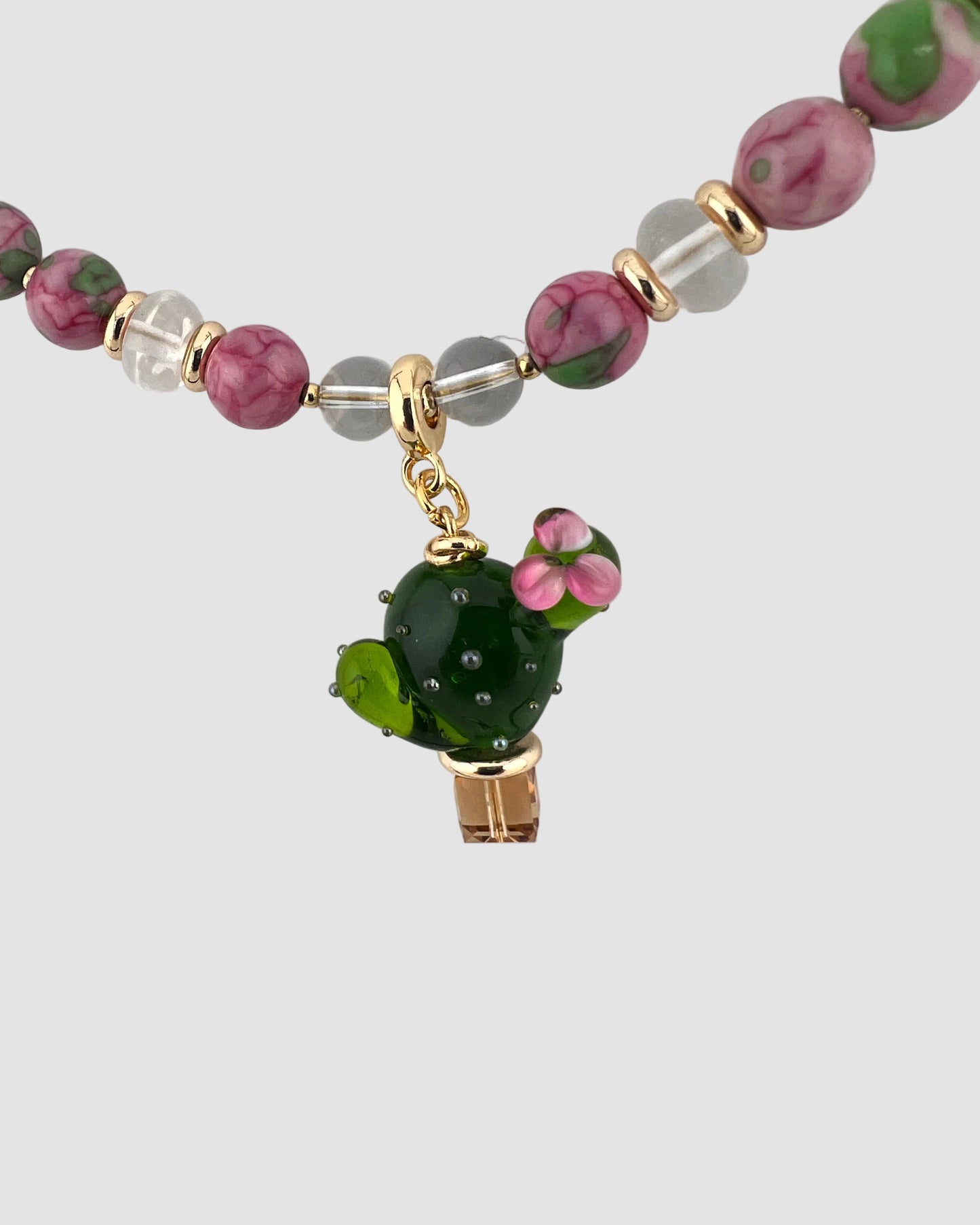 Beaded necklace with a green cactus charm on a light gray background