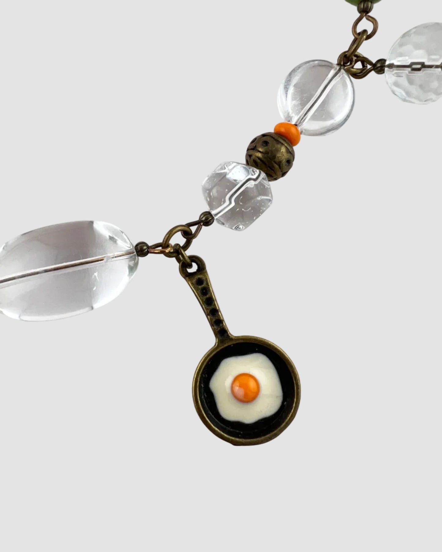 Necklace with pendant of a frying pan with an egg on a white background