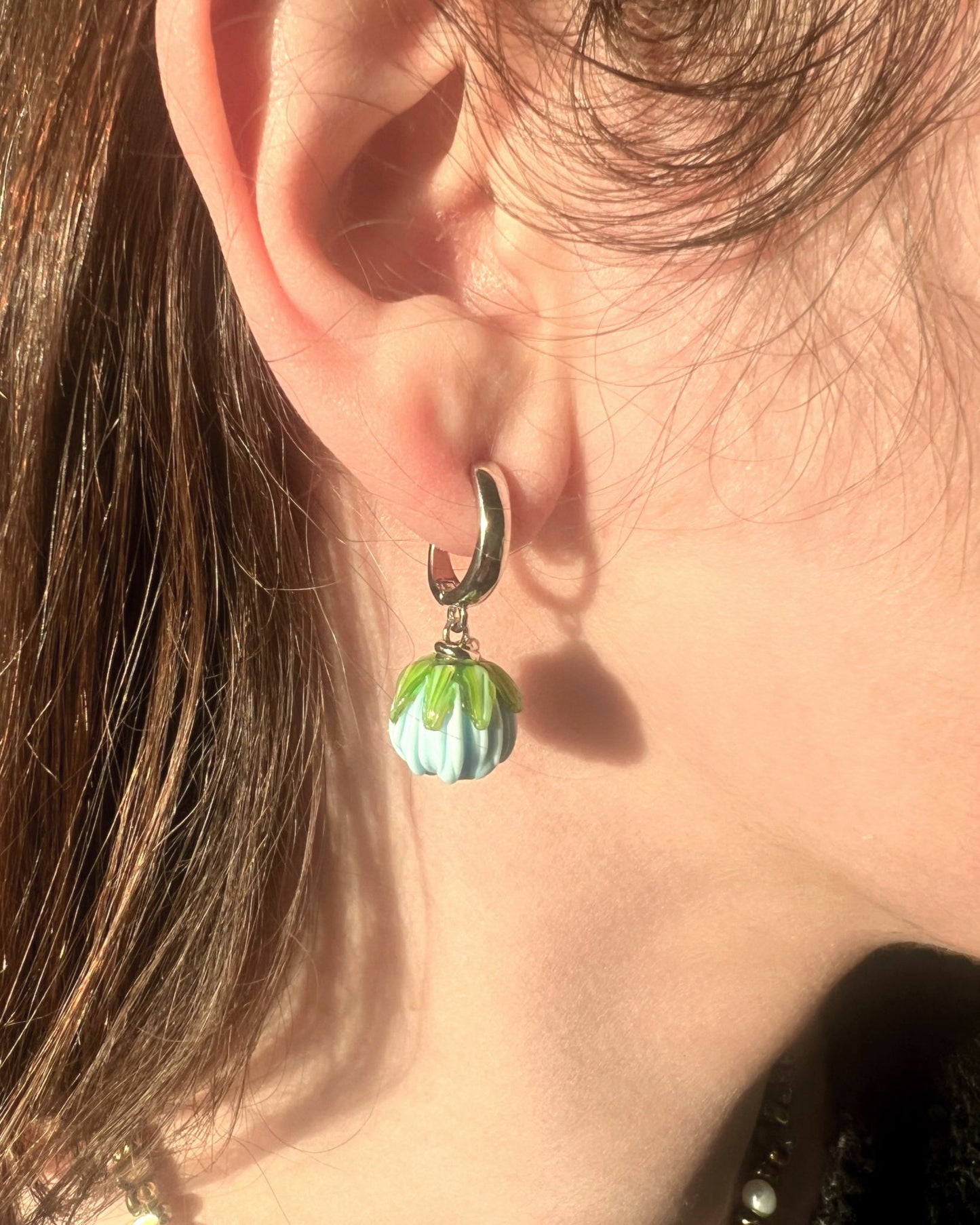 Close-up of an ear wearing a silver earring with a green and white bead.