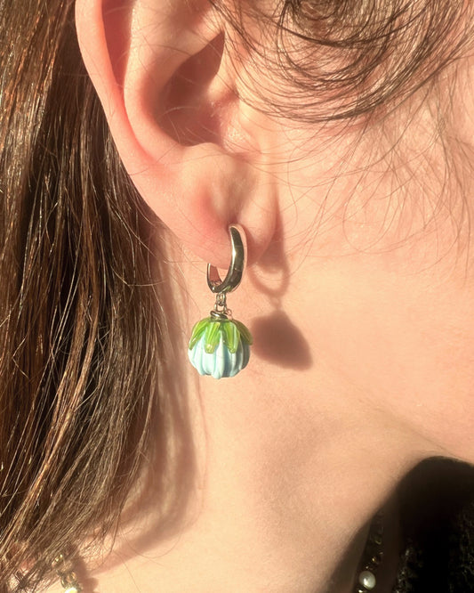 Close-up of an ear wearing a silver earring with a green and white bead.