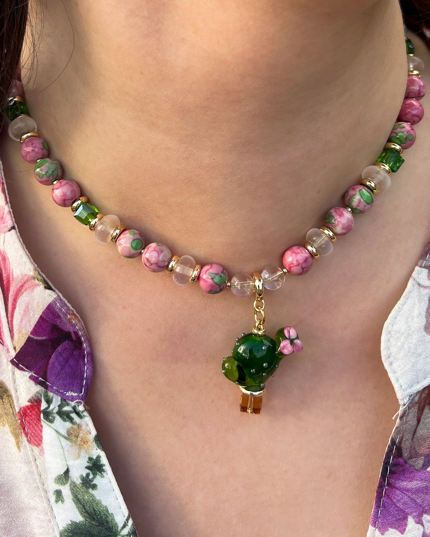 Necklace with green and pink beads and a small green flower pendant on a person wearing a floral top.