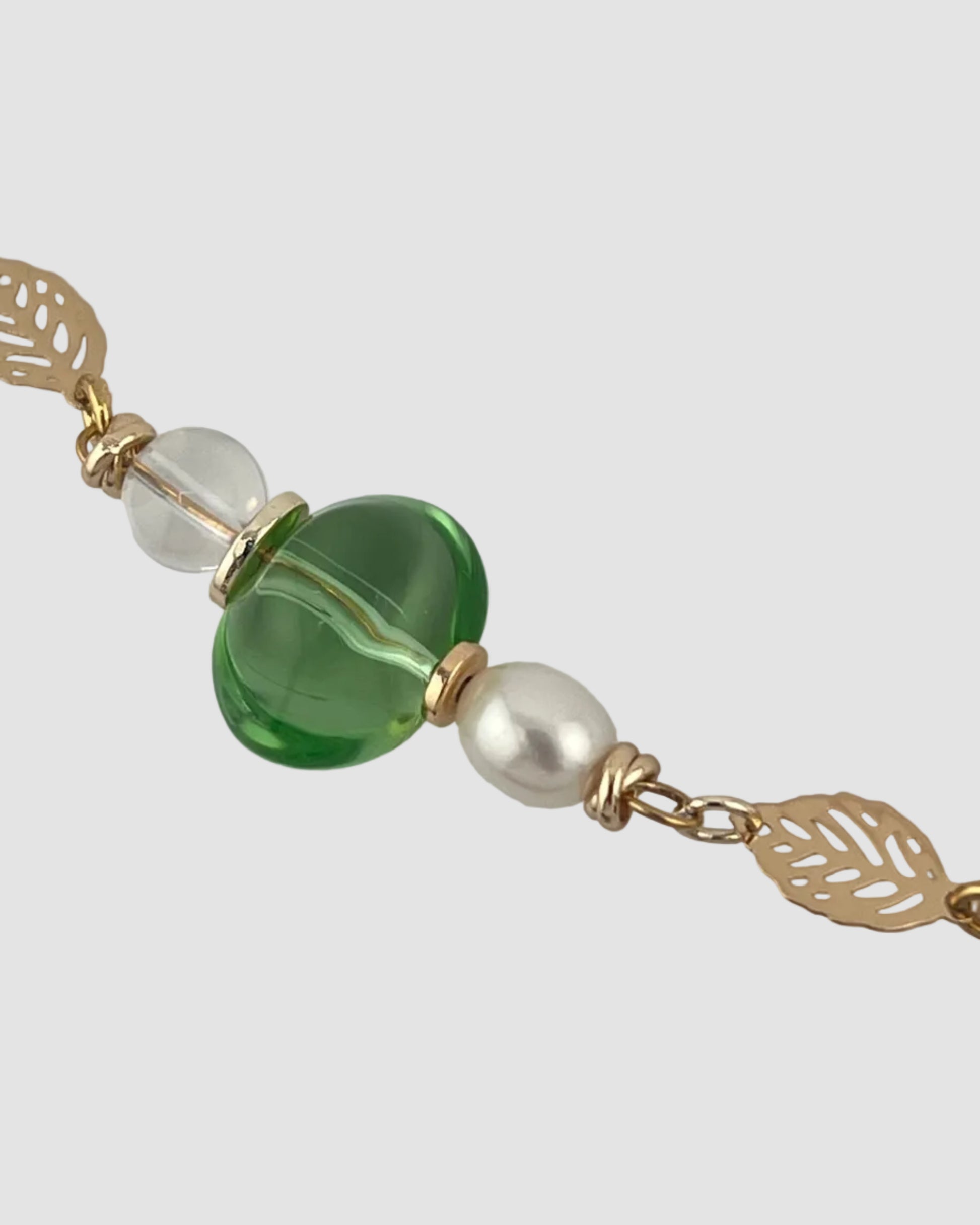 Close-up of a keychain with green beads and gold accents on a light gray background