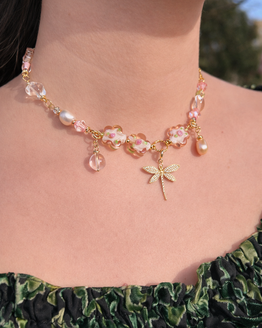 Necklace with pink beads and a dragonfly charm worn by a person.