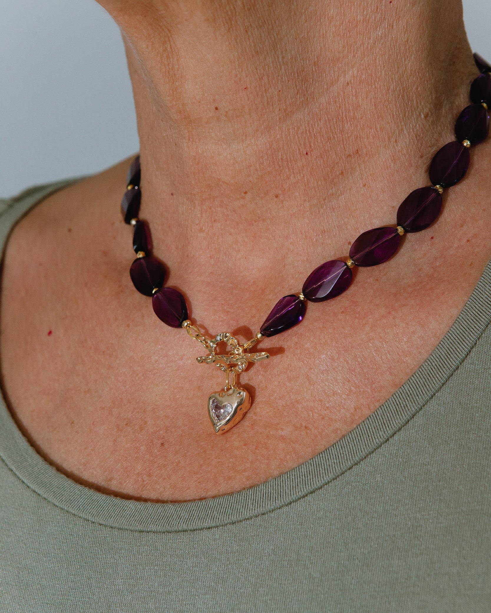 Necklace with purple beads and a gold charm worn by a person