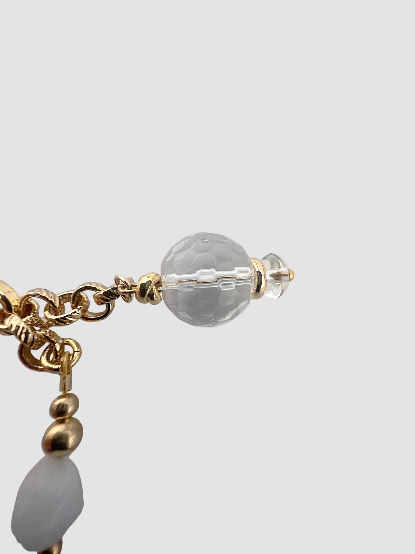 Close-up of a gold and crystal beaded earring on a light gray background