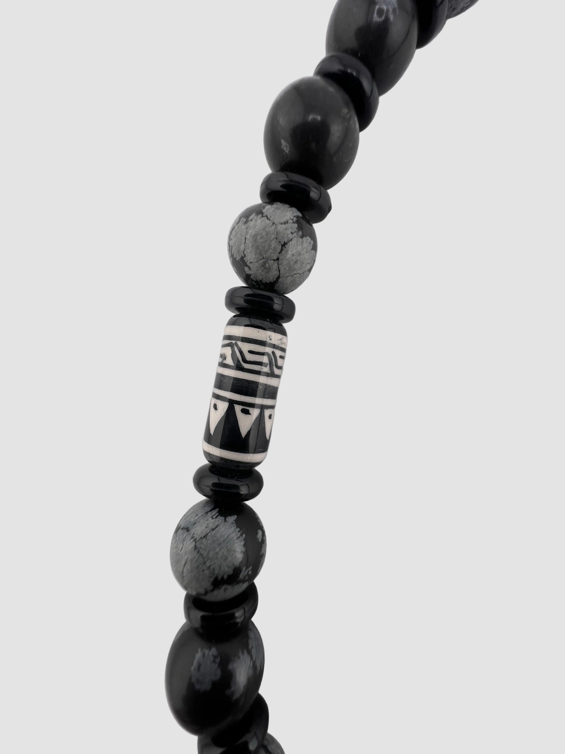 Black beaded necklace with a patterned focal bead on a white background