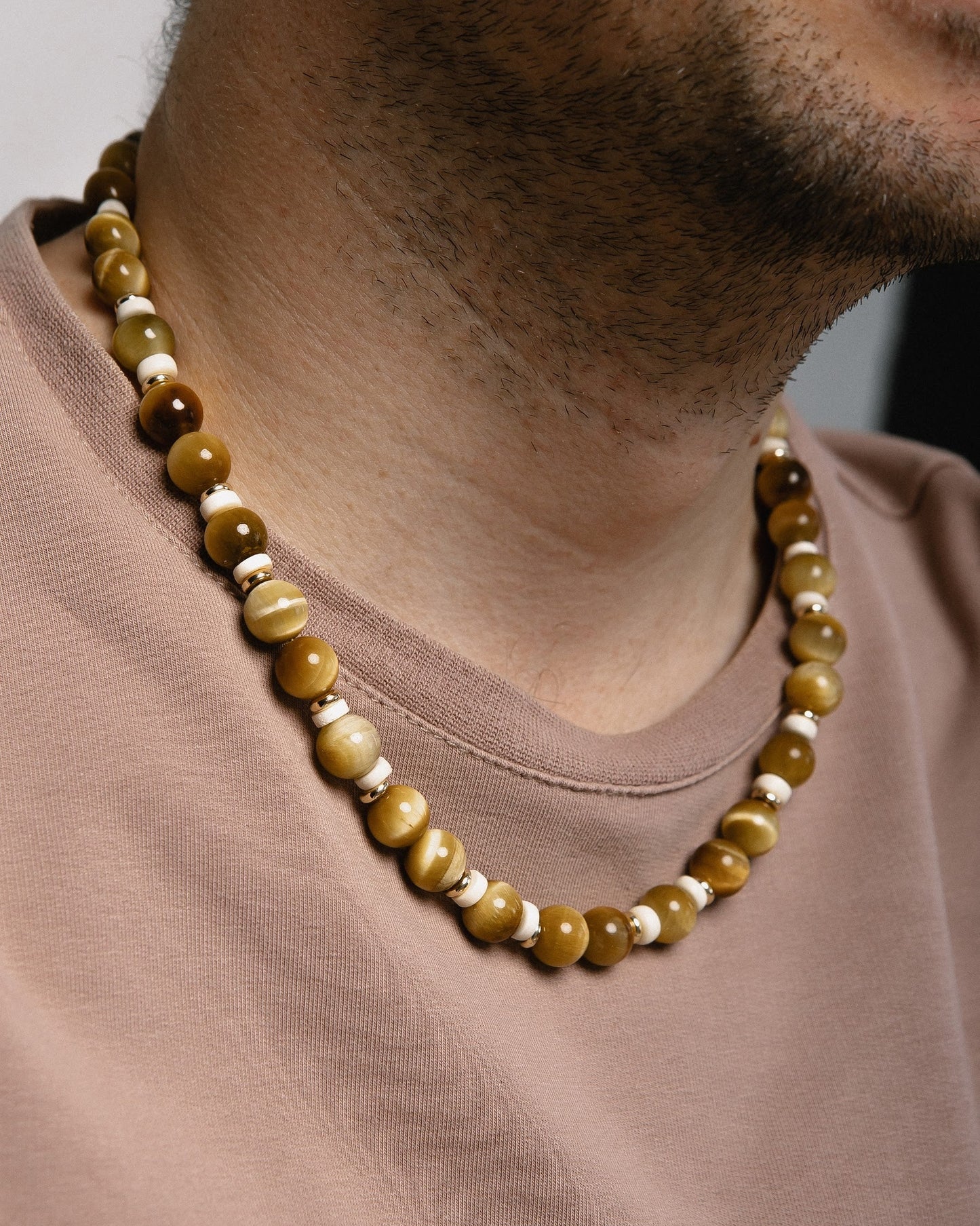 Necklace with brown and beige beads worn by a person in a brown shirt.