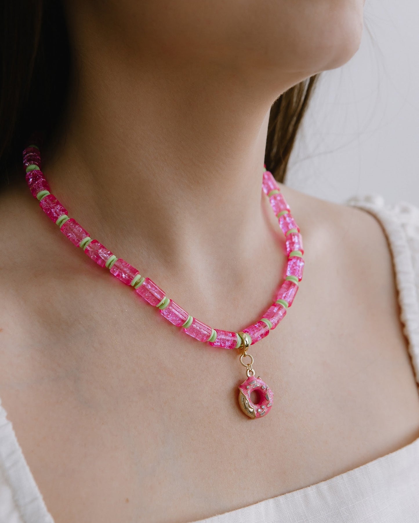 Necklace with pink beads and a donut charm worn by a person