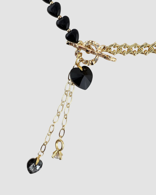Necklace with black heart-shaped beads and gold chain on a light gray background