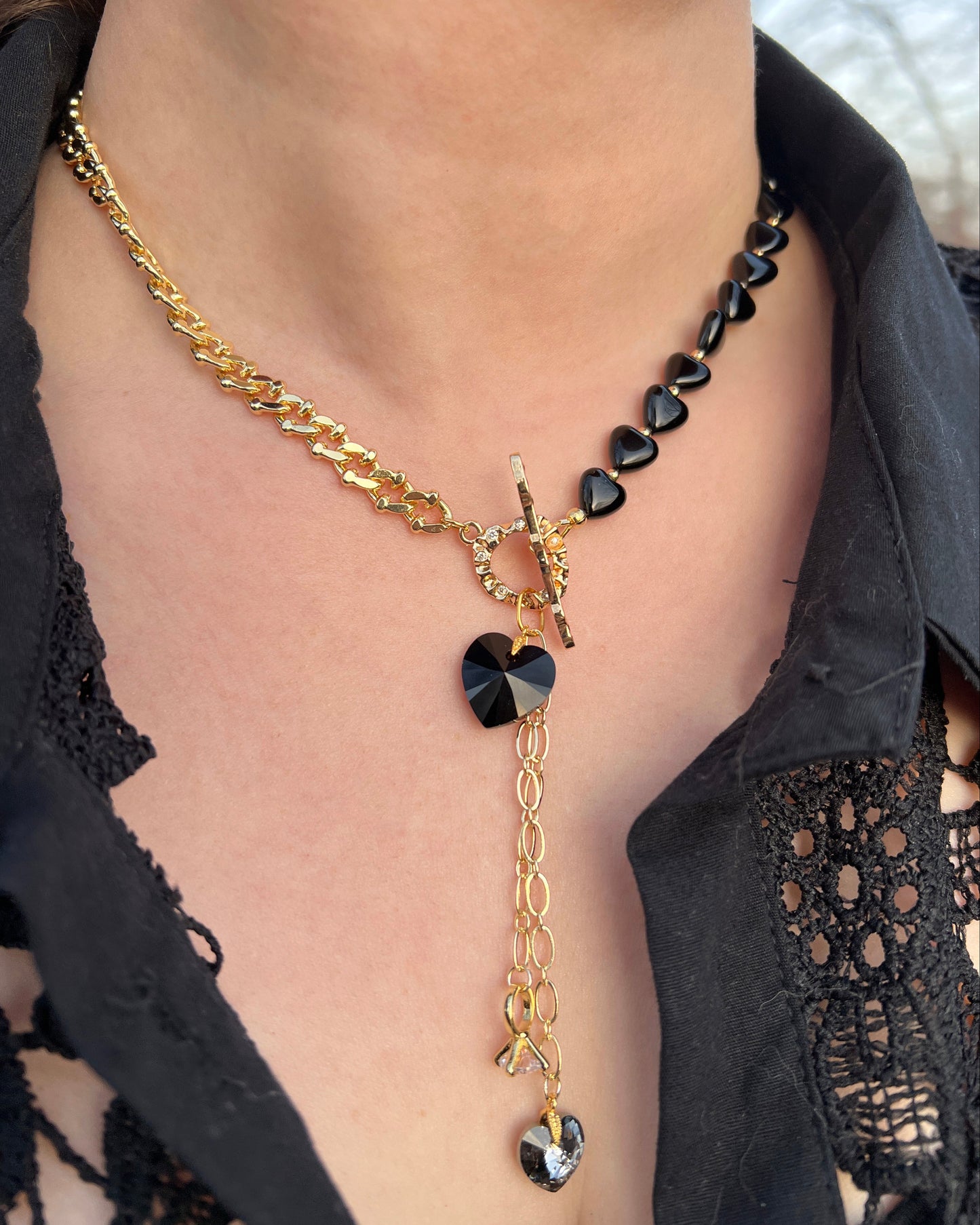 Gold chain necklace with black heart pendants worn by a person in a black lace garment.