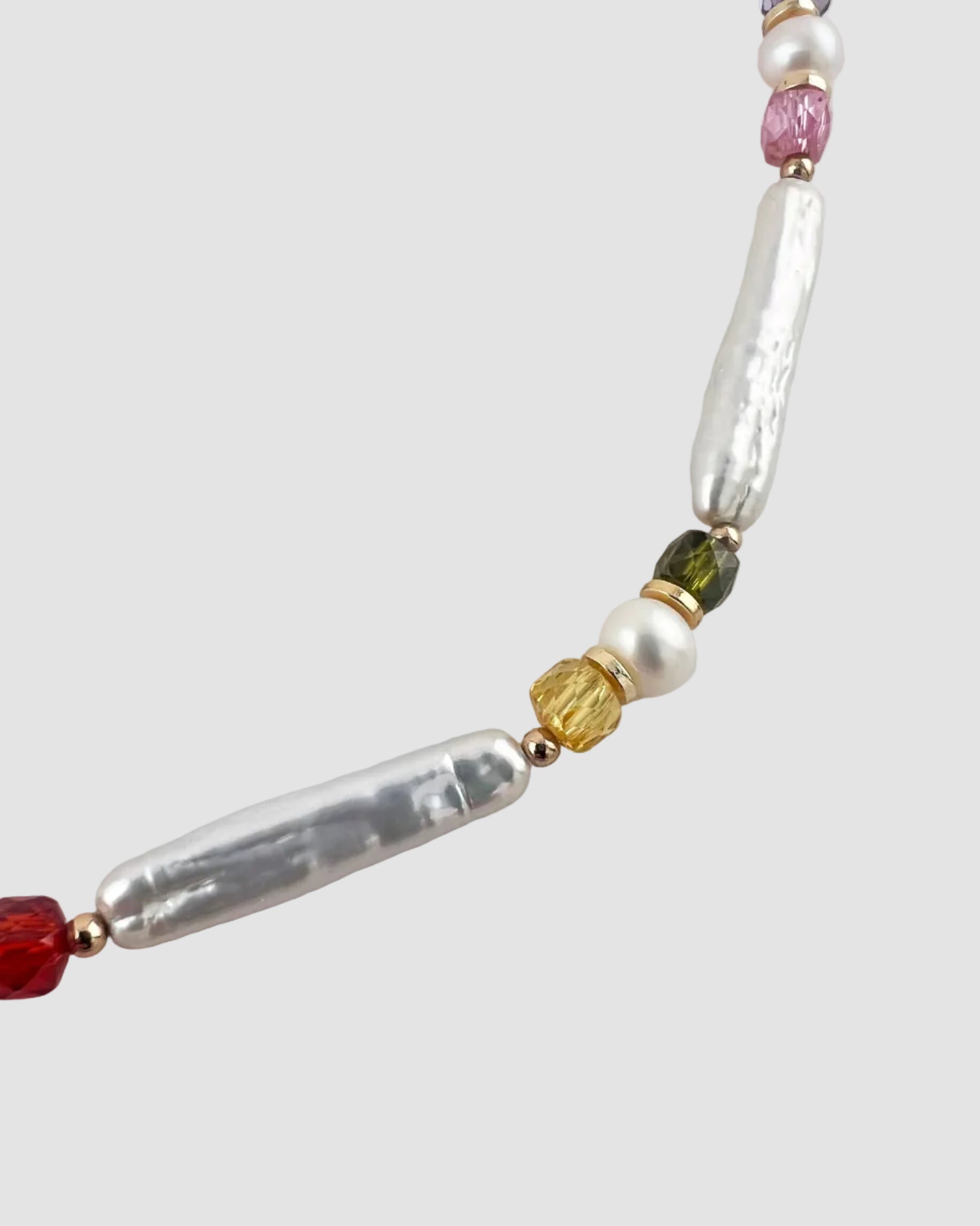 Close-up of a beaded necklace with pearl, red, green, and gold beads on a light gray background