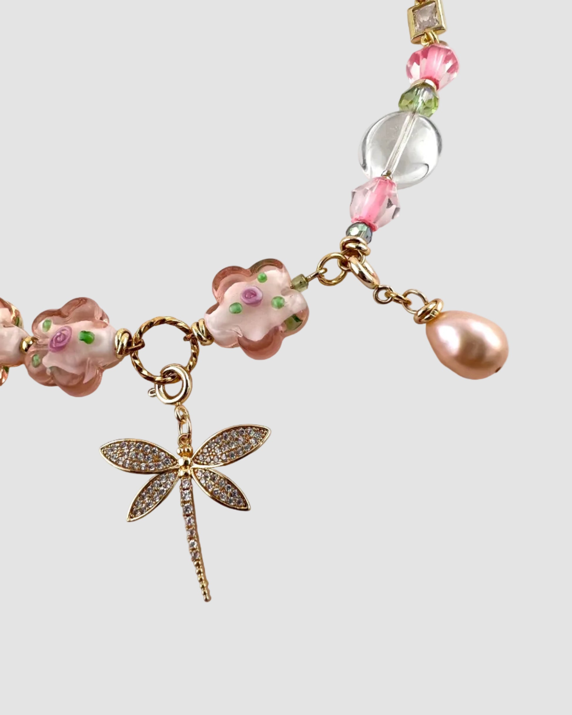Bracelet with pink beads and a dragonfly charm on a light background