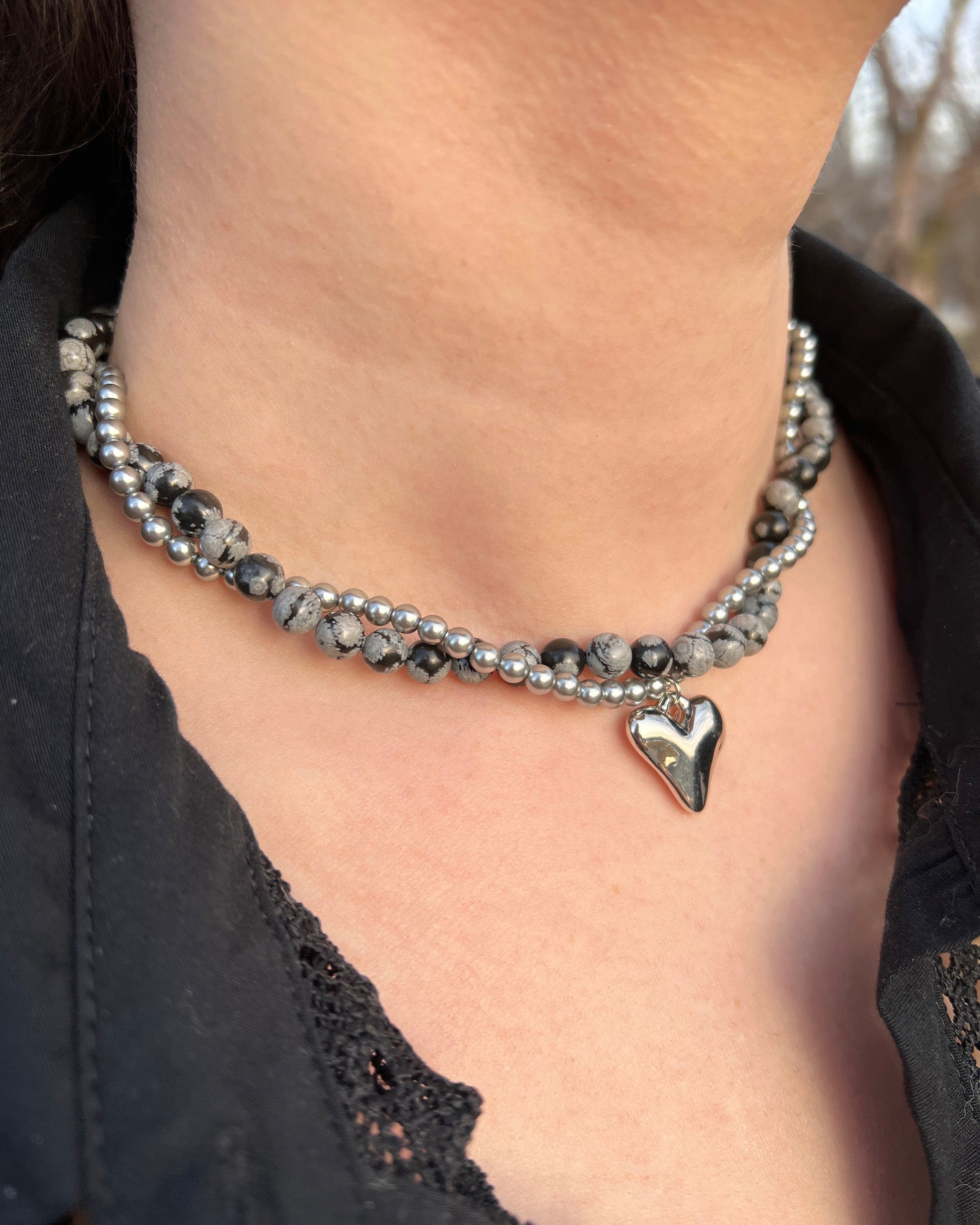Close-up of a person wearing a beaded bracelet with a heart charm on a black lace garment.