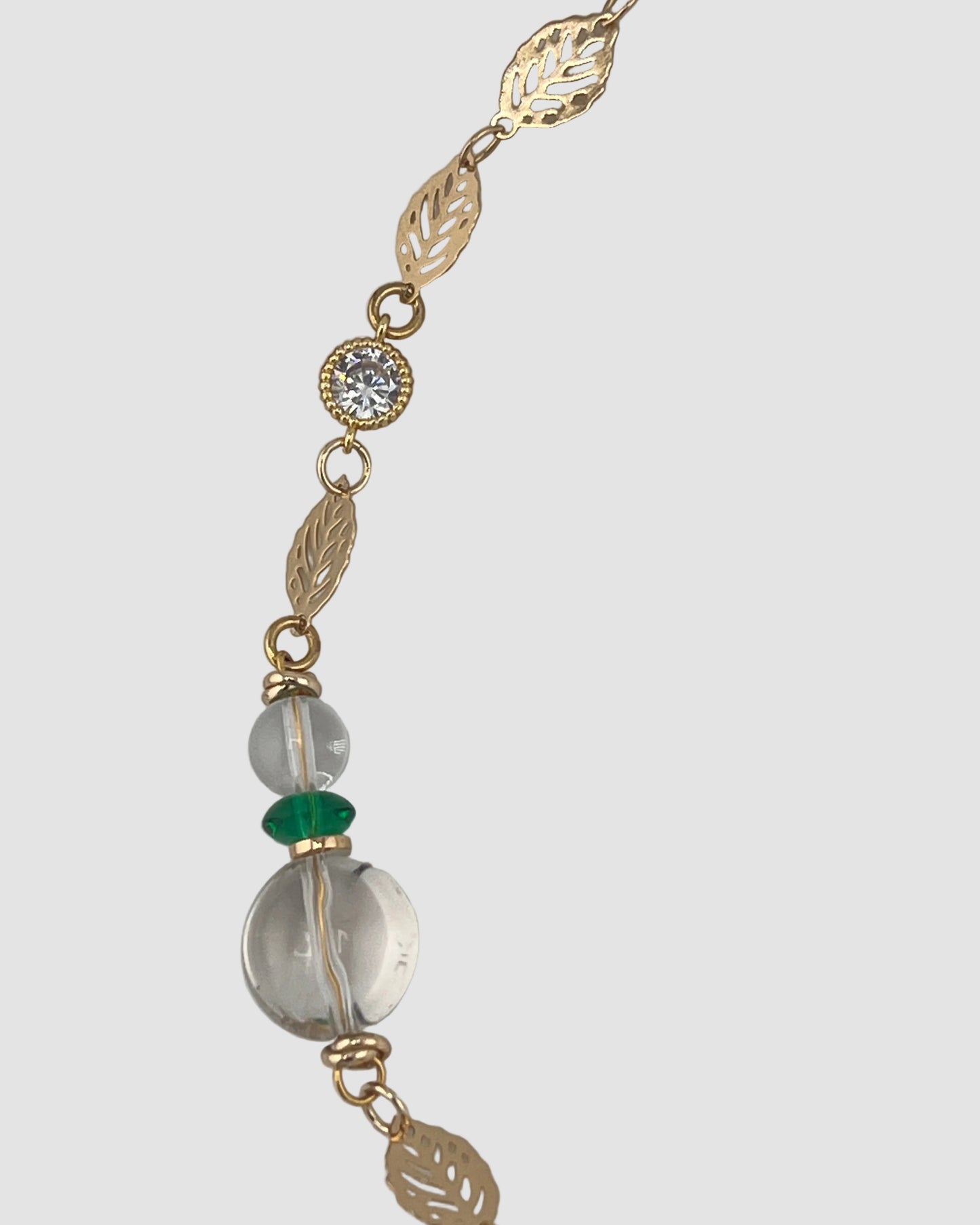 Gold chain necklace with clear and green beads on a gray background