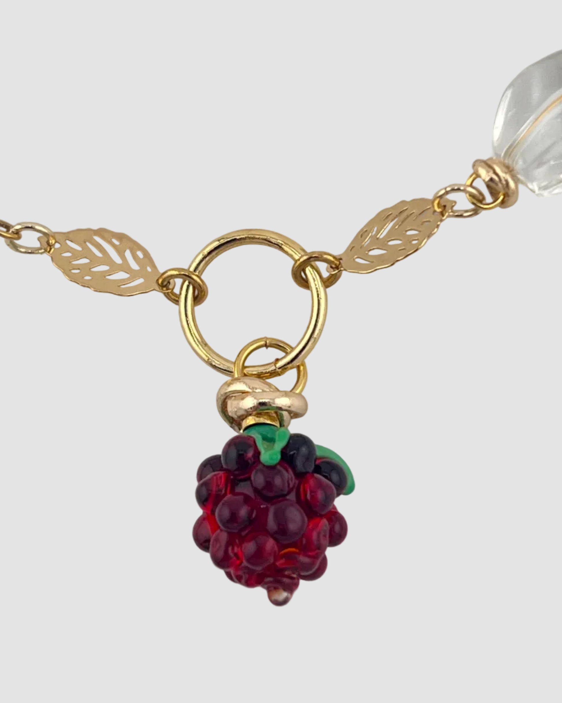 Gold chain necklace with a red berry charm on a light gray background