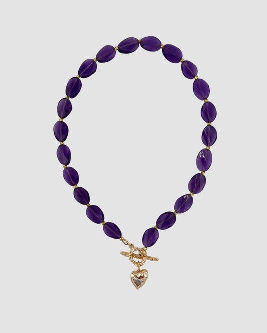 Purple beaded necklace with a gold heart pendant on a white background