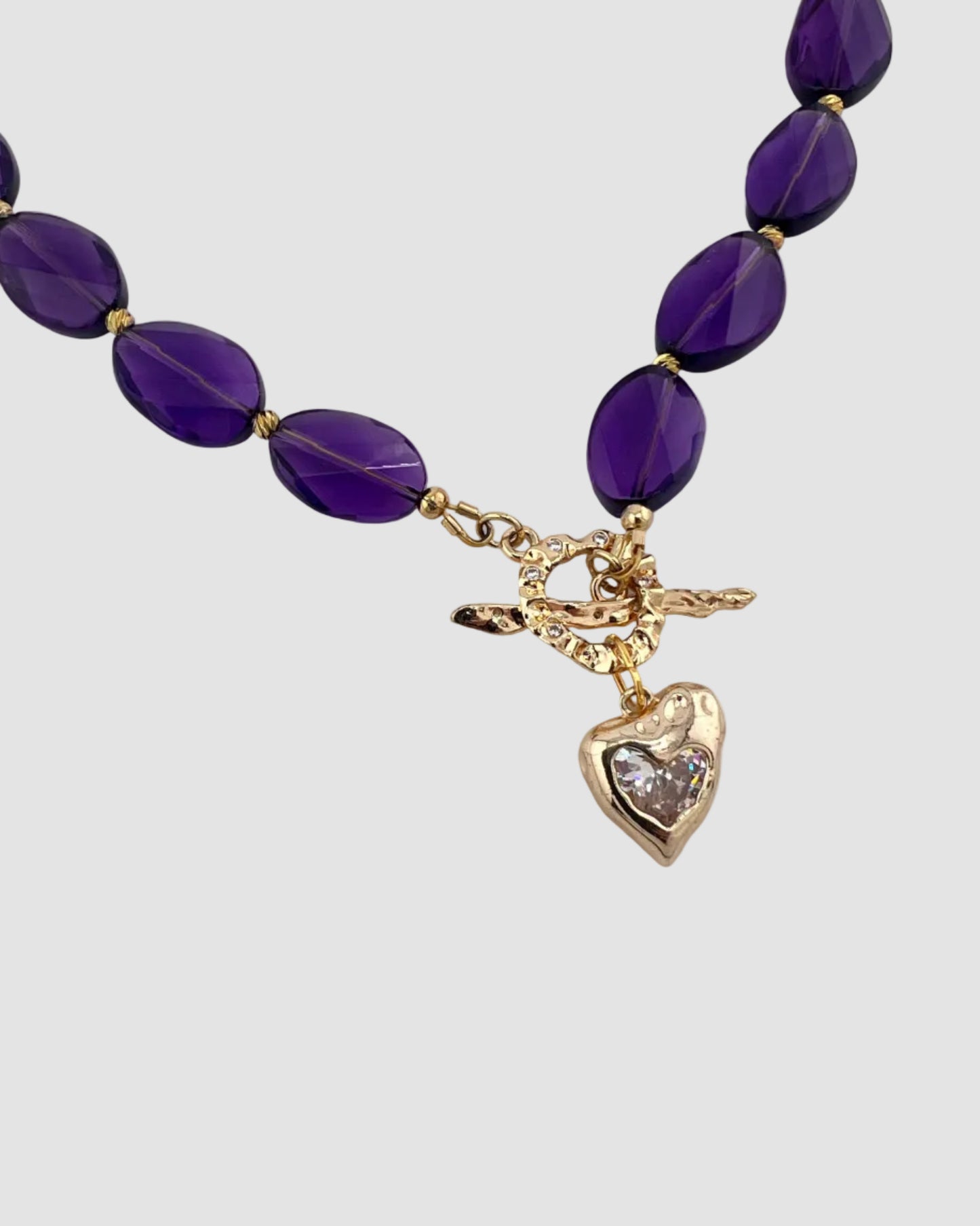 Purple beaded necklace with gold heart charm on a white background