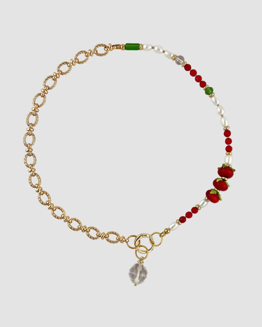 Nacklace with gold chain, red and green beads on a light gray background